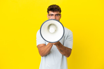 Young caucasian handsome man isolated on yellow background shouting through a megaphone to announce something