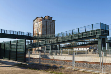 Fototapeta na wymiar Old silo and pedestrian walkway over fenced train track 