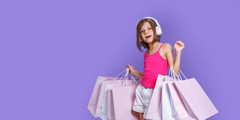Portrait Of Joyful Teen Girl Wearing Headphones and Shopping Bags Over Purple Background