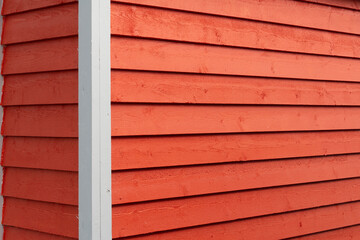 The exterior of a bright orange narrow wooden horizontal clapboard wall of a house. The trim on the...