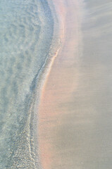A band of waves snake covers the pink sand, view from above.