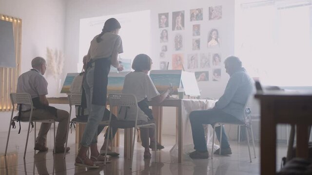 Side view of a happy senior people smiling while drawing as a recreational activity or therapy in paint class together with the group of retired women and men