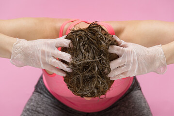 Naklejka premium Home beauty industry in coronavirus pandemic time. young woman in gloves stays at home and painting her hairs on pink background