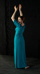woman in blue-green long dress on black background dancing