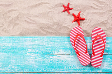 Fototapeta premium Red starfish and flip flops on the sand and wooden board top view