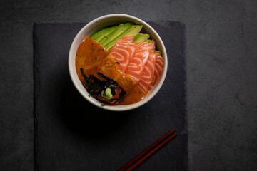 Salmon poke bowl with avocado and seaweed spicy sauce Japanese style. Top view on black table background. Asian trendy food.