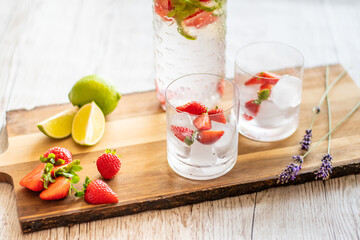 Fresh drink with strawberry and lime placed on wooden desk. Glasses with lemonade and ice. Summer drink.