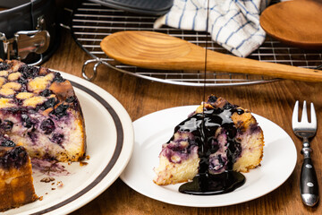 Pouring topping chocolate on a piece of delicious homemade blueberry and crumble cheesecake.