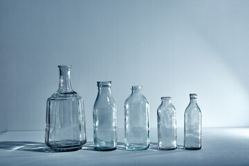 A five different empty glasses bottles with copy space. Graphic still life with light and shadow in blue light. The concept of containers, recyclable materials or alcoholism. Creative vintage vase