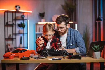 Father with son in protective glasses using soldering iron for repairing red toy car at home....