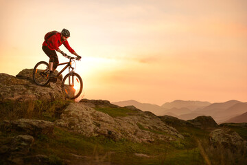 Obraz na płótnie Canvas Cyclist in Red Riding Bike on the Summer Rocky Trail at Sunset. Extreme Sport and Enduro Biking Concept.