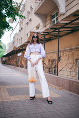 a beautiful girl with oranges in a knitted bag, white trousers and a blouse in the city