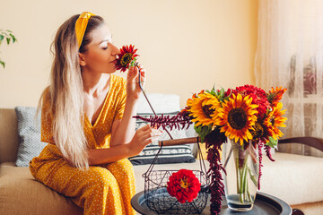 Woman smells sunflower arranging bouquet with zinnia flowers in vase at home. Lady enjoys fresh...