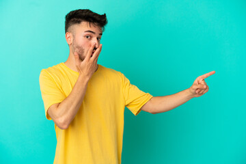 Young caucasian man isolated on blue background with surprise expression while pointing side