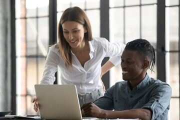 Smiling multiracial employees brainstorm cooperate using modern computer discuss company business ideas or project together. Caucasian businesswoman help African American colleague in office.