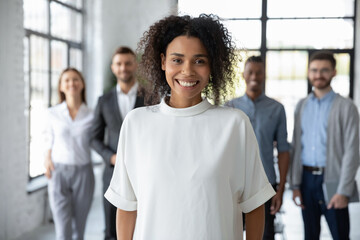 Portrait of smiling young African American female employee or worker forefront satisfied with new job position. Happy millennial ethnic biracial woman pose in office. Diversity, employment concept.