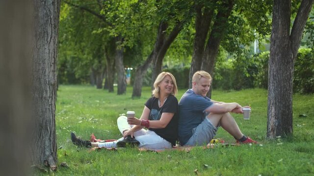 Smiling Middle-Aged 50s Woman with her Adult Son Chatting and Drinking Tea or Coffee while Resting in a Park. Slow Motion. Bonding and Family Reunion, Mothers Day Concept