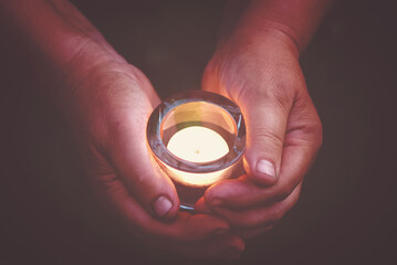 hands holding burning candle in the dark, prayer and spirituality concept