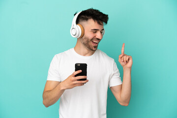 Young caucasian man isolated on blue background listening music with a mobile and singing