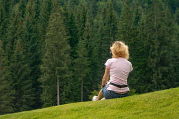 Young woman sitting on the grass and looking at the mountain forest.
