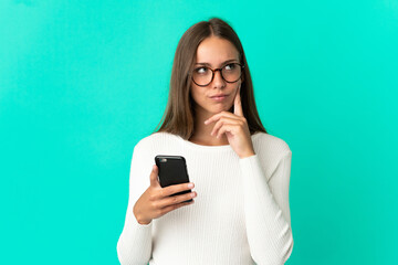 Young woman over isolated blue background using mobile phone and thinking