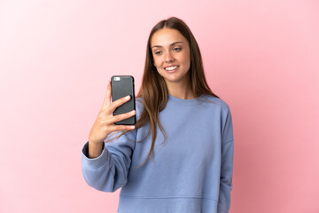 Fototapeta premium Young woman over isolated pink background making a selfie