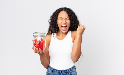 hispanic pretty woman shouting aggressively with an angry expression and holding  red liquorice...
