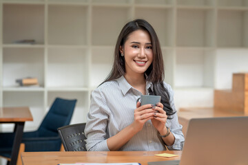 Beautiful young Asian businesswoman sitting and drinking coffee relax in the office tablet on table. Looking at camera.