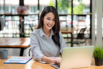 Obraz na płótnie Canvas Front view of attractive young Asian business woman sitting using laptop graph placed at the office.