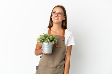 Gardener girl holding a plant over isolated white background thinking an idea while looking up