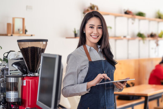 Beautiful young Asian businesswoman owner holding a tablet at a café. Looking at the camera.