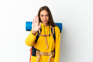 Young mountaineer woman with a big backpack over isolated white background making stop gesture