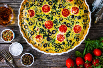 Millet quiche with spinach, black olives, cherry tomatoes and ricotta on wooden table
