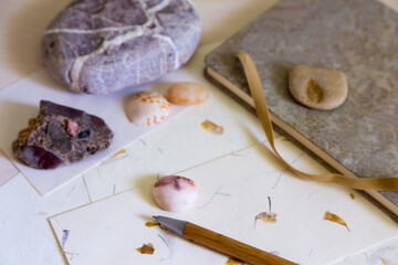 Selective focus still life of wooden pen and and handmade sheets of cream paper and envelopes with notebook, pretty rocks and a shell 
