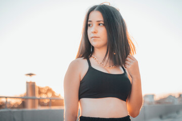 Chica joven morena junto a la puesta de sol contemplando el anochecer en la ciudad