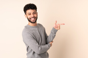 Young Moroccan man isolated on beige background pointing finger to the side