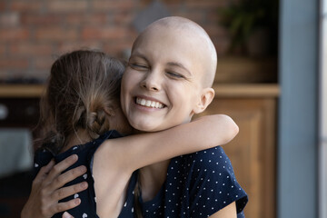 Happy excited young cancer mom embracing daughter kid. Ill mother and child hugging, celebrating...