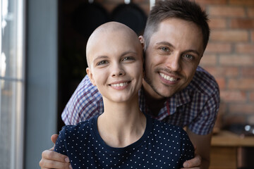 Portrait of happy young man hugging beloved woman with cancer, looking at camera, smiling. Loving...