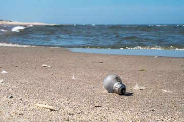 Obraz premium Garbage on the beach. A glass bulb on the seashore. Pollution of the coast.