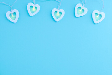 Electric white garland with glowing lights in the form of hearts on blue background. Place for your text.