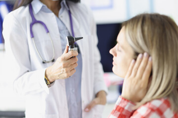 Otorhinolaryngologist examines a woman ear with otoscope - obrazy, fototapety, plakaty
