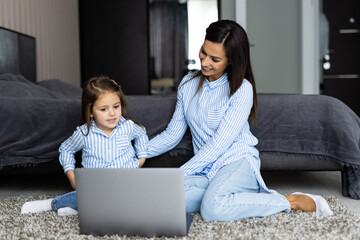 Portrait of young mother and daughter with laptop lying in bed at home