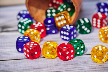 View to different colored game dices and a dice cup on a wooden table.