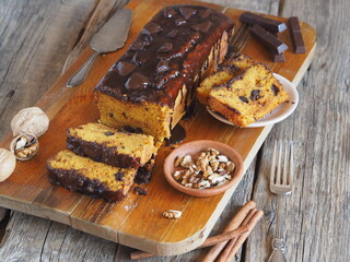 Chocolate festive pumpkin long rectangular cupcake, glazed with chocolate, ready to eat on a kitchen board with ingredients for baking. Wooden background.