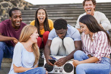 Young multiracial people using smartphone and listening music from boombox vintage stereo in the city - Millennial friends having fun together outdoor