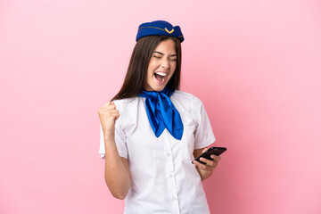 Airplane stewardess Brazilian woman isolated on pink background with phone in victory position