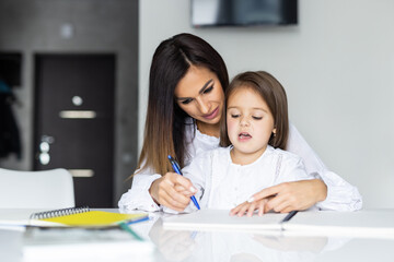 Mother teaching daughter how to write in the kitchen