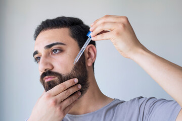 Bearded man holding pippete with beard oil