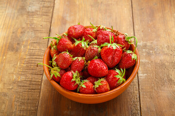 Ripe strawberries in a wicker basket on a wooden background.