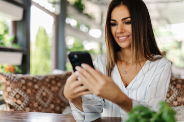Portrait of young woman use mobile phone while sitting in comfortable coffee shop during work break,